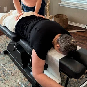 Person lying face down on a treatment table while another person places hands on the lower back area.